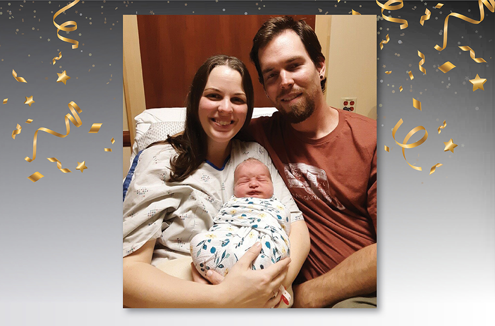 Parents Hannah and Darby Schock hold their newborn baby while sitting together in a hospital bed. Hannah wears a hospital gown.